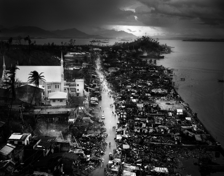 Fotoreportaż, II miejsce w kategorii "Środowisko", fot. Tomasz Gudzowaty

Miasto Tacloban, 580 km od stolicy Filipin, Manili. 8 listopada 2013 roku przez miasto przeszedł tajfun Yolanda (znany także pod nazwą Haiyan). Raport ze zwiadu lotniczego US Navy na drugi dzień po katastrofie donosił o dziesiątkach niepogrzebanych zwłok na ulicach i zniszczeniach sięgających 90 proc. zabudowy. Ogłoszono stan wyjątkowy, jednak miejscowe władze straciły kontrolę nad sytuacją. Tajfun zdewastował lotnisko. W całym regionie Visayas prawie 2 mln ludzi straciły dach nad głową. Zdjęcia ukazują sytuację w mieście trzy tygodnie po katastrofie. 28 listopada 2013